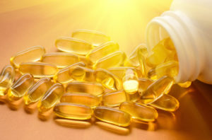 Fish oil capsules with omega 3 and vitamin D in a plastic bottle on a shiny surface with sun beams, healthy diet concept