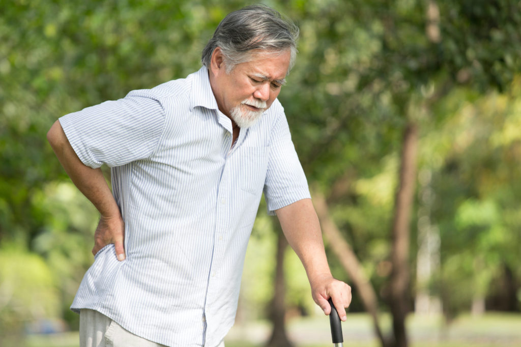 Senior Asian man suffering from back pain while he is walking outdoors