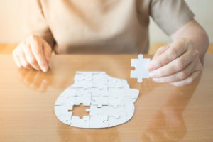 Elderly woman's hands holding missing white piece above a human head jigsaw puzzle