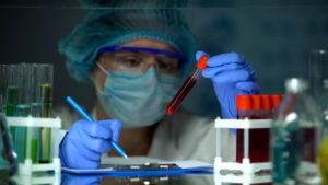 Doctor checking tube with blood analysis and making notes