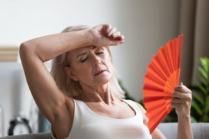 Menopause taking center stage, shown by woman fanning herself due to hot flashes.