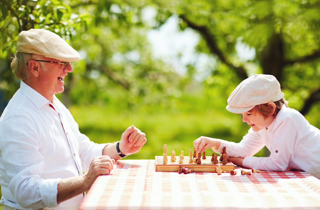 Alzheimer's Disease Prevention shown by happy grandpa and grandson playing chess in spring garden