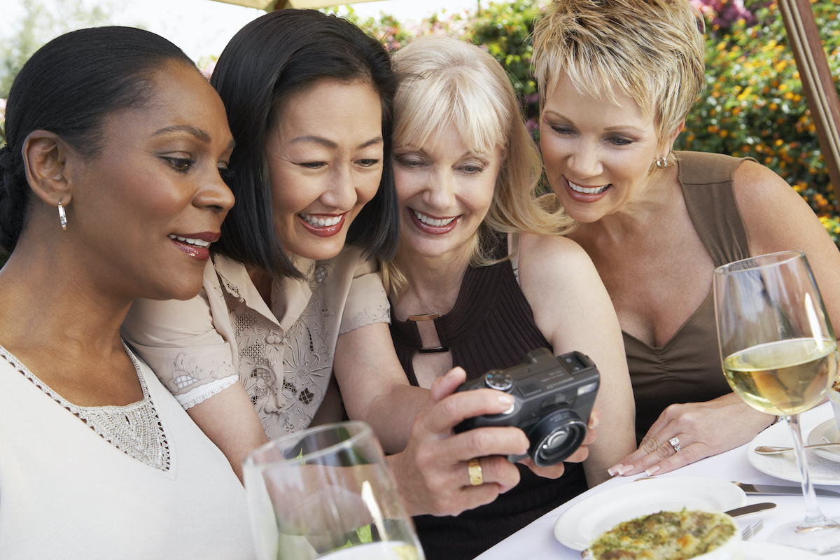 Hormones for menopause as shown by happy female friends looking at photos on digital camera