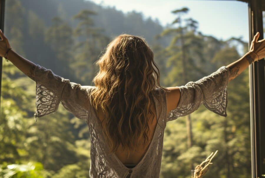 Woman recovering from lupus stands at window with arms held out