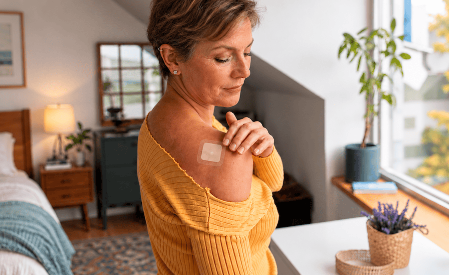 Middle aged woman applying transdermal testosterone hormone patch to shoulder.