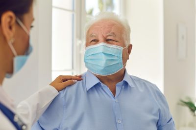 Senior patient and doctor, wearing medical face masks, communicating in hospital office.